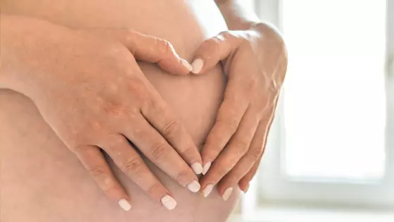 Mulher grávida repousa mãos sobre a barriga em pré-natal
